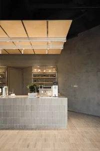 Modern minimalist cafe interior with a grey tiled concrete service counter, bonsai tree, coffee equipment, and a large floating wooden canopy with linear lighting.