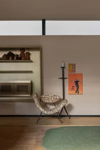 Modern minimalist living room featuring a brown and white boucle papasan-style chair, built-in shelving with terracotta pottery, black candle stand, colorful abstract wall art, and a round green rug on wooden floor.