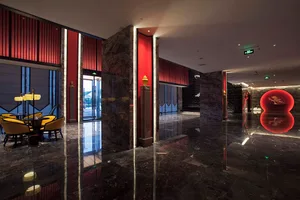 Luxurious hotel lobby featuring glossy black marble floors, bold red vertical wall panels, marble columns, and a sculptural red circular art installation in the background.