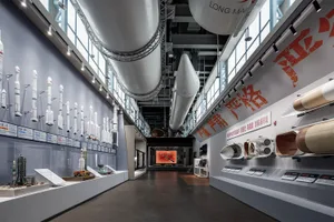 現代航太博物館展廳內部視角，牆面展示多枚全尺寸與模型火箭，大型火箭部件懸吊於天花板，明亮的軌道燈照明與詳細資訊展示板。