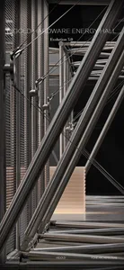 Close-up view of a modern stainless steel staircase featuring diagonal support beams, tension cables, and industrial metal railings in a contemporary exhibition hall.