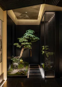 Modern indoor Japanese garden entrance with large bonsai pine tree, moss garden, stone water feature emitting mist, dark wood paneling, and vertical illuminated wooden slats.