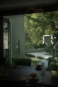Modern minimalist dining area with dark table set, looking out through large openings to a concrete courtyard with water pond and dense bamboo forest.