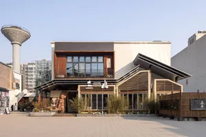 Front view of San Shan Shuan Rou Bistro showcasing a two-story building with prominent corten steel cladding, wooden slat canopies, large glass windows, and landscaped entrance with bamboo and stone sculptures.