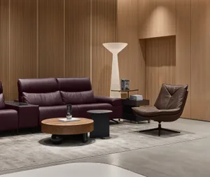 Modern living room with a burgundy leather sofa, brown leather swivel chair, round walnut coffee table, and vertical wood slat wall with a tall white floor lamp.