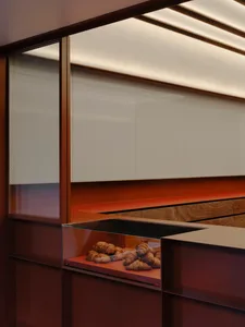 Modern bakery interior featuring a curved walnut pastry counter with glass display case filled with croissants under warm linear LED lighting.