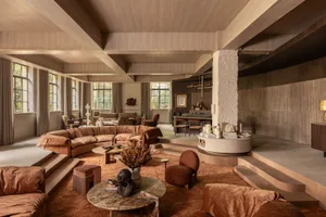 Spacious split-level living room featuring a large curved terracotta sectional sofa, raised circular terrazzo platform, warm wood ceilings, and multiple conversation areas bathed in natural light.