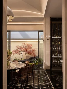 Modern luxury dining room with round marble table, velvet dining chairs, black and white patterned marble floor, and a Japanese maple tree in an indoor courtyard visible through large glass doors.
