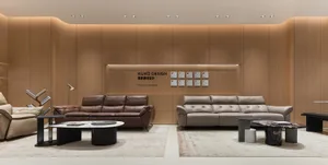 Modern living room display with a brown leather sofa and a light beige leather sofa arranged on separate area rugs in front of a curved wood-paneled wall with recessed lighting and awards.