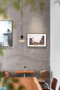 Small wooden dining table against a textured concrete wall with framed surf and Venice Beach photographs, pendant light, and wooden chairs.