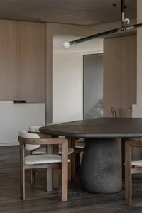 Modern dining area featuring a round dark stone pedestal table surrounded by walnut dining chairs with light bouclé upholstery, under a contemporary black pendant light.