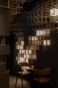 Modern restaurant dining nook featuring two leather chairs at a round table beneath a dramatic ceiling installation of illuminated brass cubes against textured dark walls.