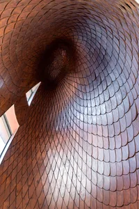 Looking up through a dramatic spiral tunnel constructed from thousands of overlapping teak wood scales arranged in a hypnotic vortex pattern.