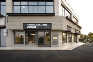 Modern corner commercial building with horizontal travertine stone cladding, large glass windows, and black textured signage for Four Seasons Coffee Livehouse.