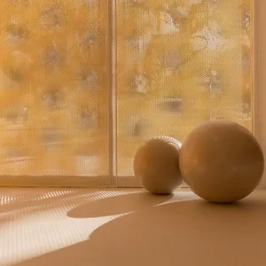 Two beige exercise balls rest on a light rubber floor in front of a glowing golden perforated screen that casts striped shadows.