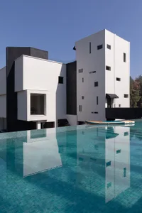 Modern white and black concrete villa with an infinity pool reflecting the building against a clear blue sky.