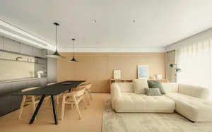 Modern open-plan living and dining room featuring a creamy white L-shaped sectional sofa, black dining table with light wood chairs, and warm wood paneling on the back wall.