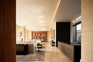 Modern luxury living room featuring large travertine stone walls, a long black marble kitchen island, a light-colored sectional sofa, and a walnut feature wall in the background.