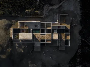 Aerial photograph of a contemporary stone courtyard villa featuring multiple infinity pools, open-air living spaces, and interconnected stone pavilions set in a rocky, arid terrain.