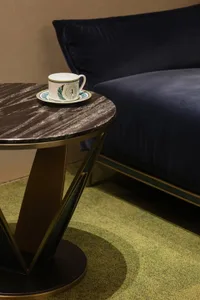 Close-up of a round dark marble side table with brass base holding a decorative teacup, next to a navy blue velvet sofa on a lime green textured carpet.