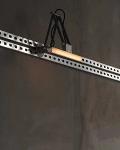 特寫鏡頭顯示一盞現代工業壁燈，發出溫暖光芒的管狀燈泡，安裝在黑色關節臂上，固定於鍍鋅鋼軌道，背景為原始混凝土牆。
