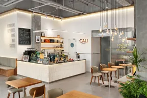 Modern minimalist cafe interior with white tiled counter, wooden tables and chairs, concrete pillars, and numerous hanging Edison bulb pendant lights.