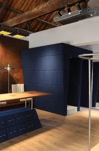 Modern dining area featuring a large navy blue velvet modular booth, light wood dining table, white leather chairs, textured brown accent wall, and exposed wooden ceiling beams with track lighting.