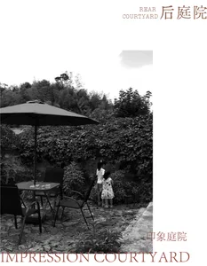 Black and white photograph of a rear courtyard featuring a stone-paved patio, black patio furniture under a large umbrella, dense ivy-covered walls, and two young girls observing the lush greenery.
