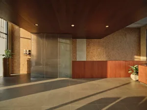 Modern commercial reception area with dark wood ceiling, warm wood paneling, beige mosaic tile walls, polished concrete floor, and potted plants.