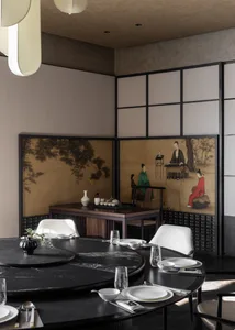 Modern dining room featuring a large round black marble table with lazy Susan, white upholstered chairs, and a striking multi-panel Chinese folding screen displaying classical ink paintings of scholars.