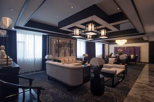 Modern luxury living room featuring dark wood ceiling beams, white sofas, marble floor, large Buddha statue, and crystal chandelier.