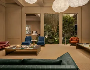 Modern living room featuring a large indoor garden wall, blue velvet armchairs, an orange leather armchair, a dark green leather sofa in the foreground, and large woven pendant lights.