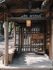 傳統中式木構庭院入口，搭配石板地面、懸掛紙燈籠、低矮木長椅與圓形坐墊，以及通往陽光充足內院的視野。