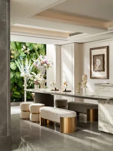 Luxurious modern entryway with white marble console table, upholstered benches, classical sculptures, and a large tropical green living wall with colorful floral arrangements.