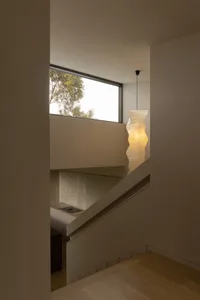 View of a modern minimalist staircase with light oak treads and risers, a built-in marble-clad niche below a large window, and a tall sculptural white paper pendant lamp hanging in the corner.