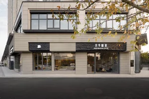 Modern coffee shop exterior with light travertine stone facade, large glass windows, and black textured stone signage reading Four Seasons Coffee.