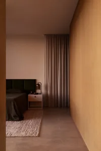 Modern minimalist bedroom featuring a dark green velvet headboard, walnut wood wall paneling, concrete floor, and neutral-toned curtains.