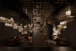 Modern restaurant interior featuring textured concrete pillars, brown leather dining chairs, round tables, and an intricate ceiling and wall installation of illuminated golden metal lattice cubes.