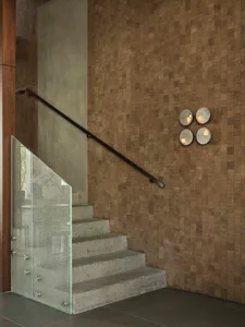 Modern concrete staircase with textured glass railing beside a wall covered in small wooden blocks and four circular wall sconces.