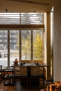 Modern Chinese-style dining room featuring dark wood table, woven rattan dining chairs, warm wooden flooring, and large glass doors opening to a lush bamboo garden with natural daylight.