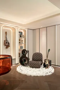 Modern luxury music corner with brown tufted lounge chair, white fluffy rug, electric guitar, acoustic guitars mounted on wall, and large horn speakers in a built-in illuminated shelving unit.