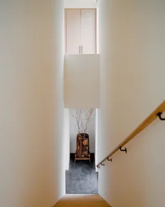 Looking down a minimalist white staircase with light wood flooring, a wooden handrail, and a large dried branch arrangement in a tree stump planter at the landing.