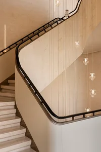 Modern curved travertine staircase with black metal handrail and multiple crystal pendant lights hanging in a vertical cascade against a textured beige wall.