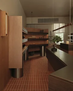 Modern minimalist home office featuring extensive walnut wood cabinetry, built-in desk, terracotta floor tiles, and a bonsai tree by the window.