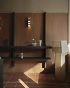 Modern minimalist entryway with dark walnut floating shelves, warm wood paneling, terracotta tiled floor, and a sculptural alabaster floor lamp illuminated by natural sunlight.