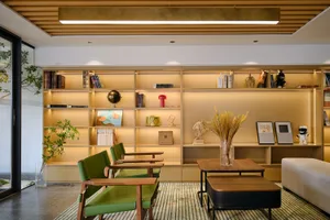 Modern living room with a large illuminated wooden built-in bookshelf wall, two green leather armchairs with wooden frames, a low wooden coffee table, and a striped area rug.