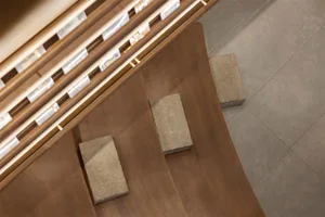Close-up overhead view of a modern wooden staircase featuring warm walnut steps and textured stone treads, with integrated LED lighting along the handrail.