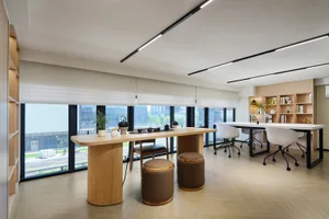 Bright modern home office featuring a solid oak tea table, brown leather ottomans, white office chairs, built-in bookshelves, and large windows overlooking the city.
