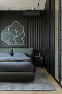 Modern dark-toned bedroom with sage green upholstered bed, large cloud-shaped artwork in teal on black wall, wood herringbone floor and grey area rug.