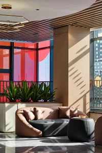 Modern lobby lounge featuring a curved two-tone leather sofa, dark ottoman, wooden slat ceiling, and large windows with red circular art installation.
